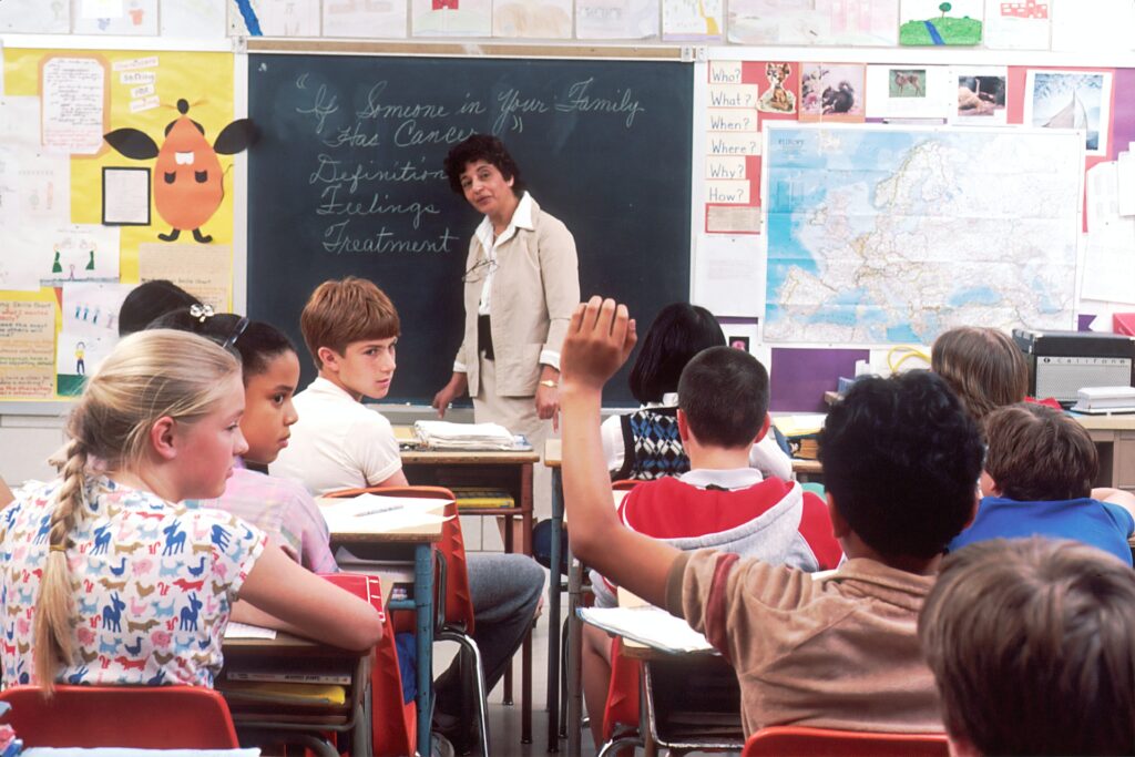 A teacher in front of a classroom with children at their desks.