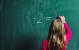 Child writing a simple math problem on a chalkboard